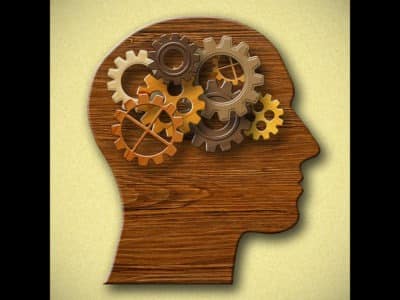 Wooden silhouette of head with brown-tone gears running inside where brain would be
