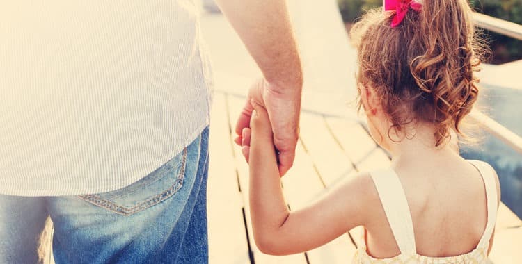 Father and young daughter wearing ponytail holding hands walking across a bridge