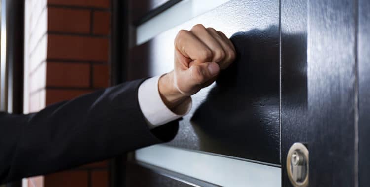 arm of person wearing a suit knocking on the door to someone's home