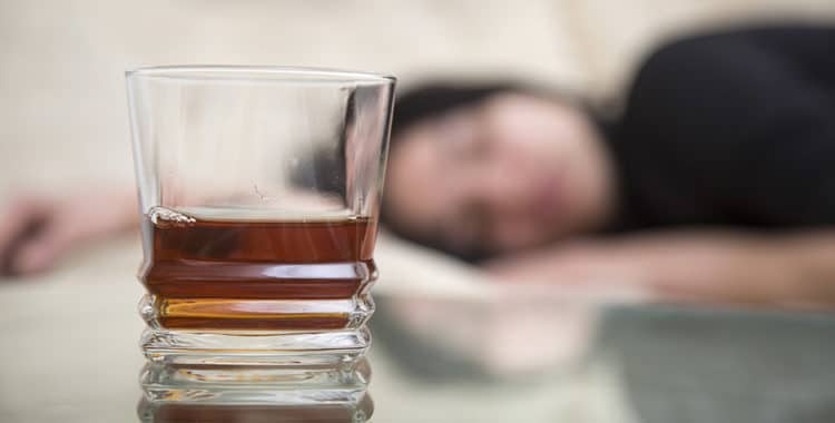 Drunk girl lying in blurry background and glass of alcohol on the table in foreground