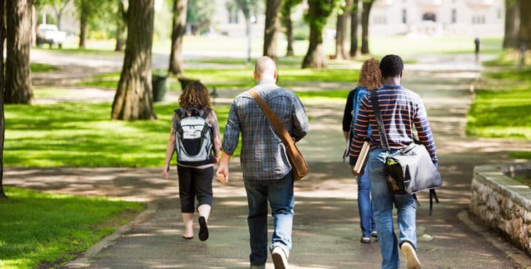 Rear view of university students with backpacks walking on campus road