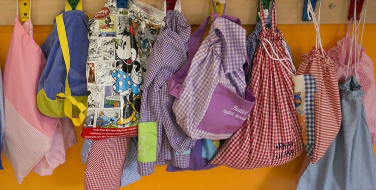 children's backpacks and jackets hanging on a row of hanging posts at a daycare