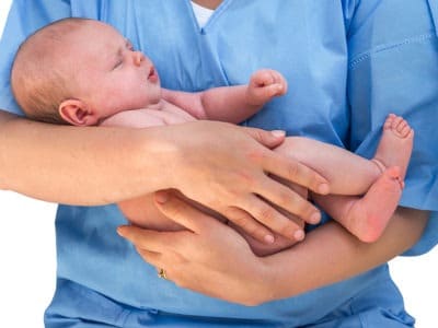 female nurse in blue scrubs holding newborn baby