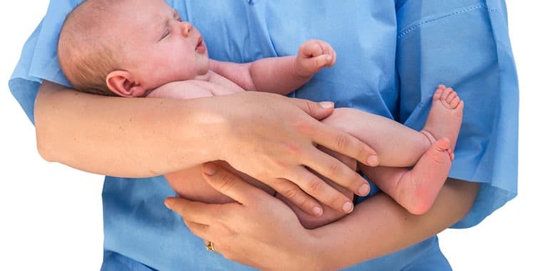 female nurse in blue scrubs holding newborn baby