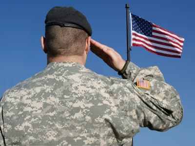 back view of soldier in camouflage uniform saluting American flag
