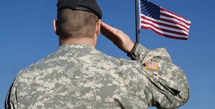 back view of soldier in camouflage uniform saluting American flag