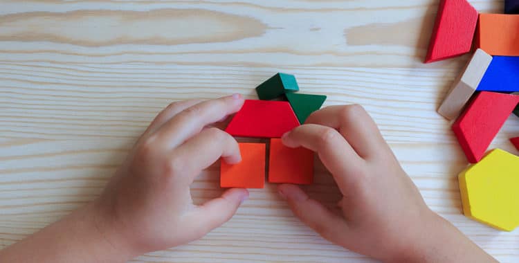 child playing with colored blocks constructing a model on a light wood table