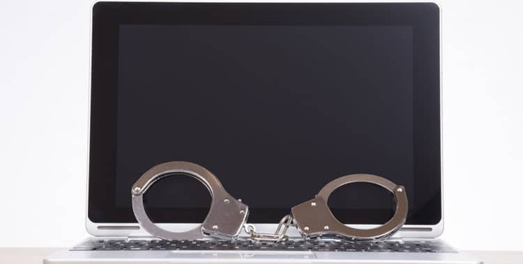 Pair of handcuffs resting on the keyboard against a blank laptop screen