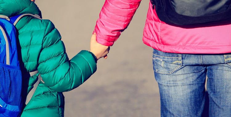 Big sister holding hand of little brother with backpack on the road