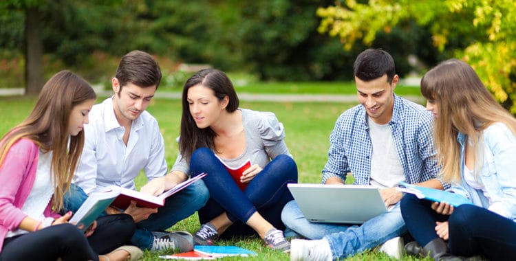 Group of college students sitting on grass in the park doing homework