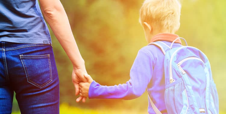 Mother holding hand of young son wearing backpack outdoors