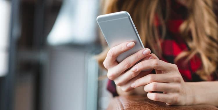 Close-up of smartphone used by blonde teenage girl in plaid shirt