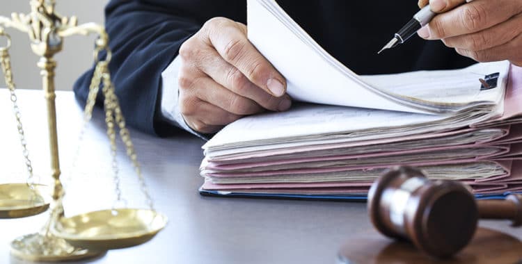 Judge filling out paperwork with scales of justice and gavel on table