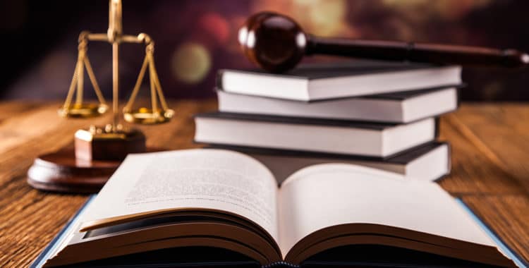 Open book in foreground with gold scales of justice and gavel resting on pile of books in background