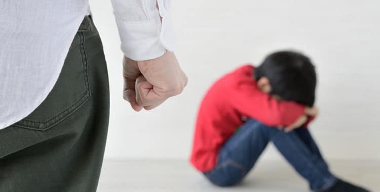 clenched fist of adult with blurry child sitting with head down in background