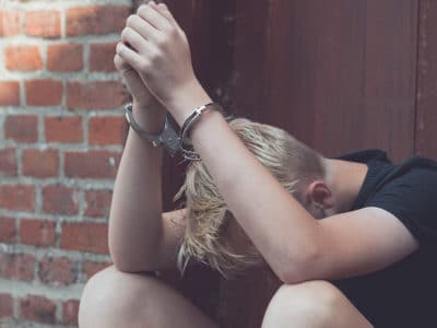 Caucasian teen sitting on ground with head down and elbows on knees wearing handcuffs