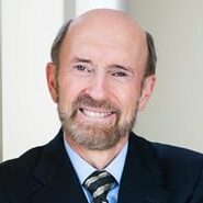 Head shot of David Marshall wearing navy blue suit with light blue shirt and gray and gold striped tie